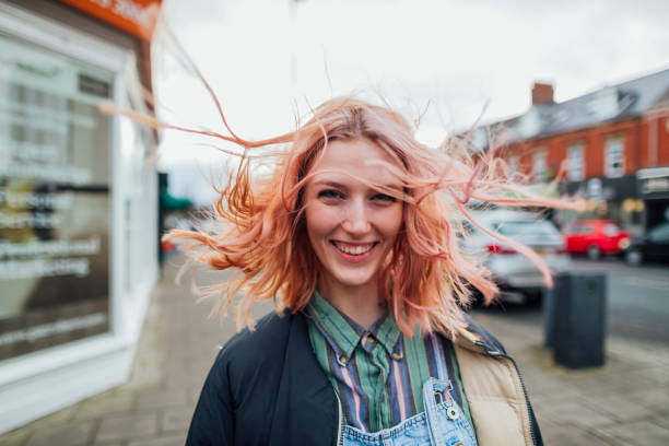 Woman standing outdoors looking away from the camera while her hair blows in the wind.